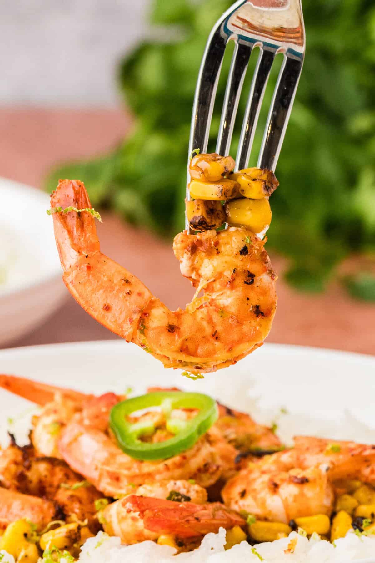 A fork holding a piece of shrimp and some corn.