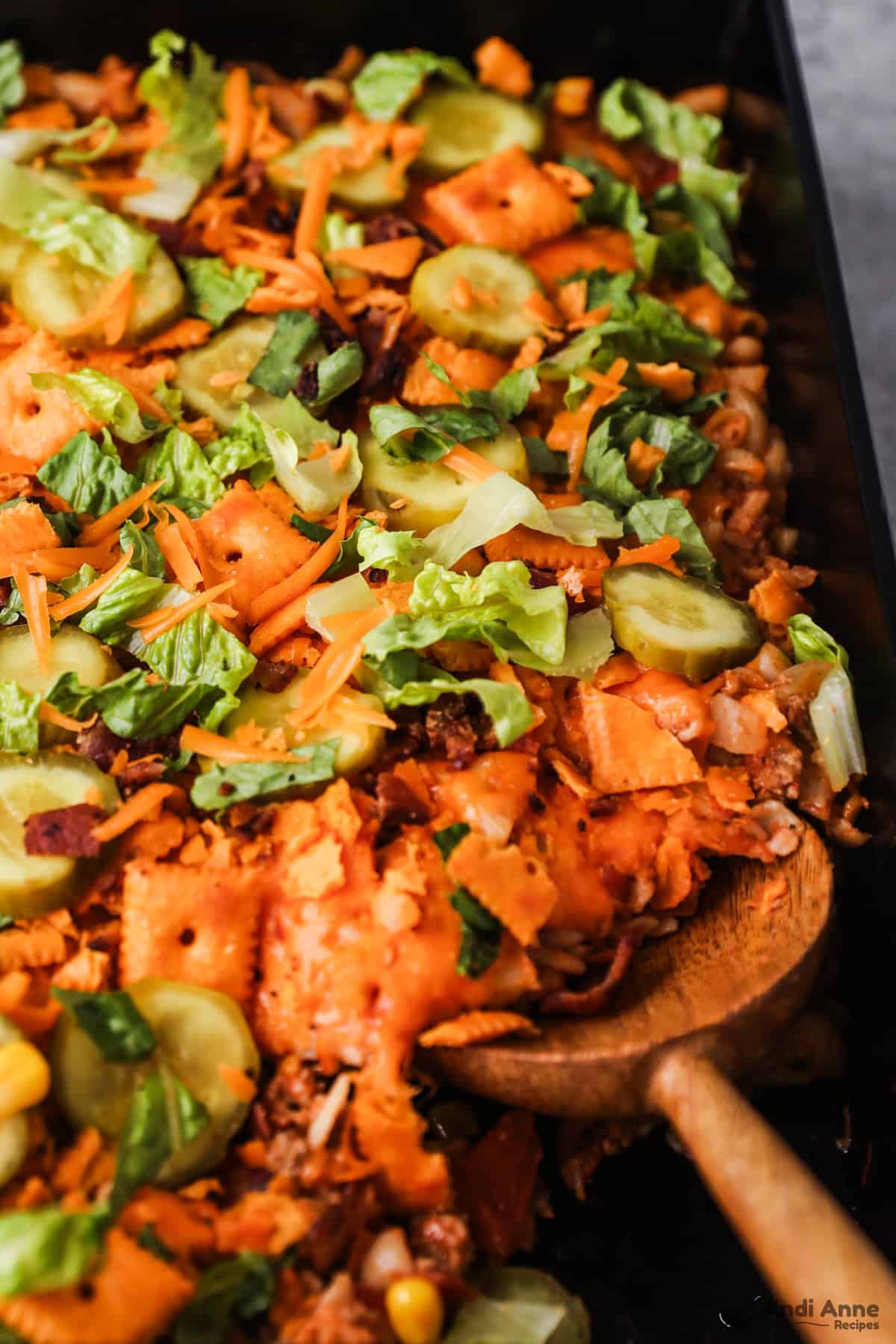 A wooden spoon is scooping a serving of cheeseburger casserole from the pan.
