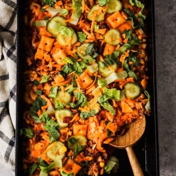 A pan of cheeseburger casserole topped with pickle slices and lettuce.