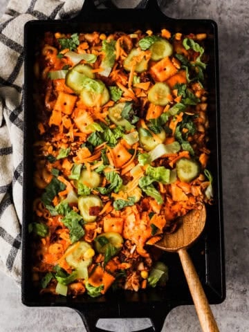 A pan of cheeseburger casserole topped with pickle slices and lettuce.