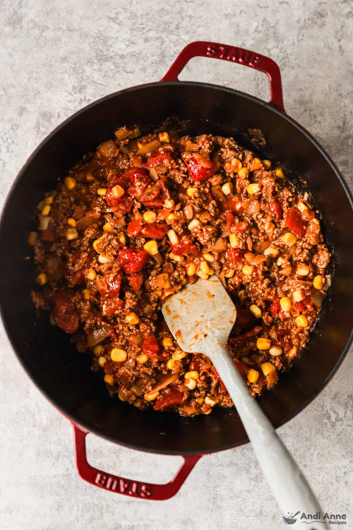 A pot of ground beef, spaghetti sauce, tomatoes, corn, and seasonings.