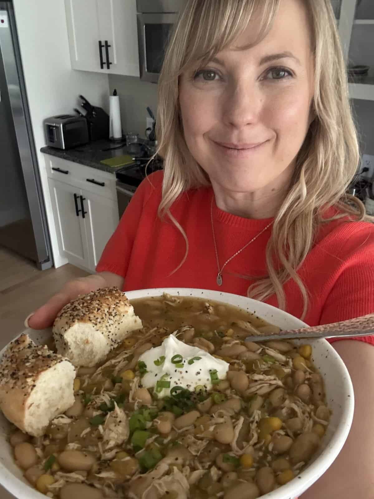 Andi is holding a bowl of white chicken chili with a bun on the side.