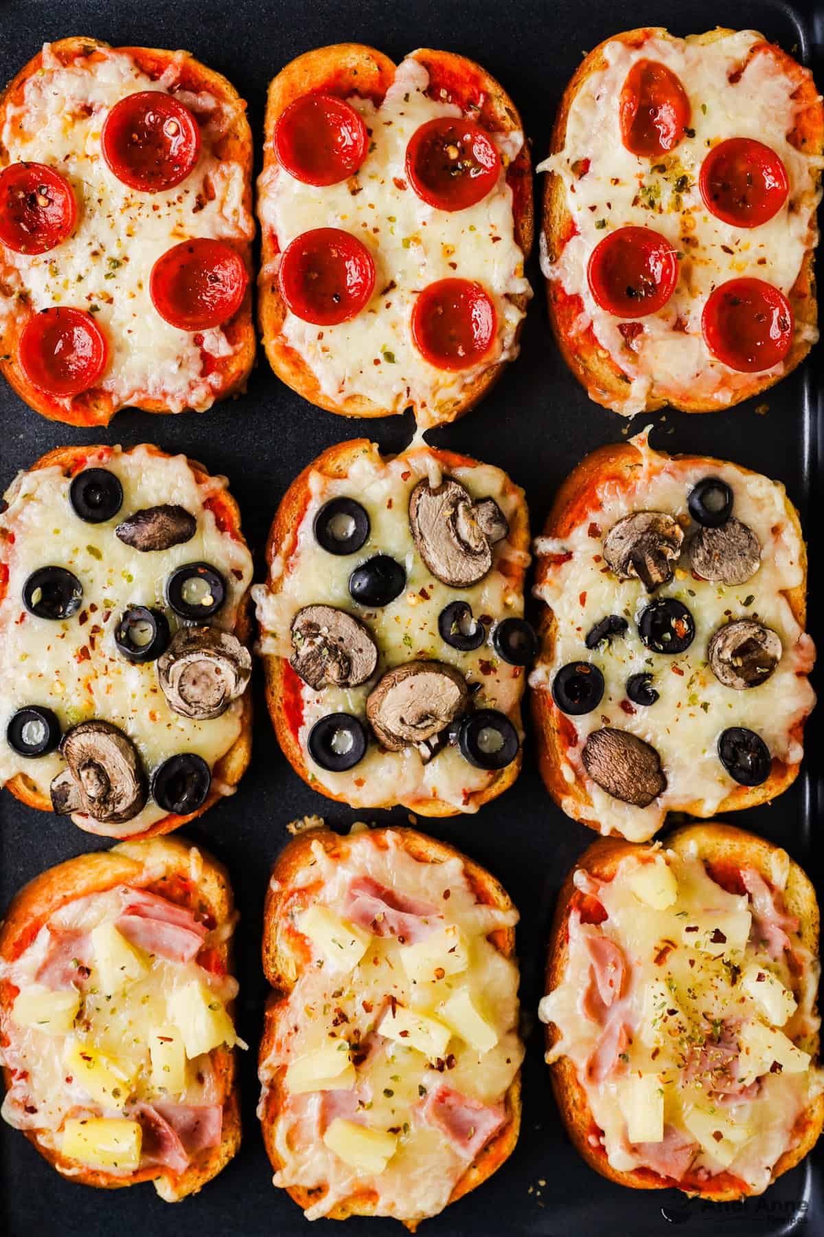 A baking sheet with pepperoni, olive and mushroom, and ham and pineapple garlic toast pizzas.