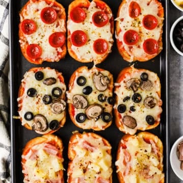 A baking sheet with pepperoni, olive and mushroom, and ham and pineapple garlic toast pizzas.