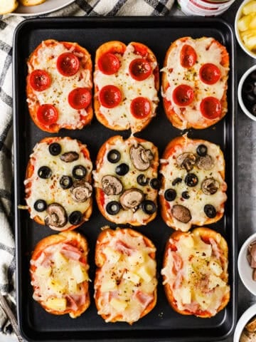 A baking sheet with pepperoni, olive and mushroom, and ham and pineapple garlic toast pizzas.
