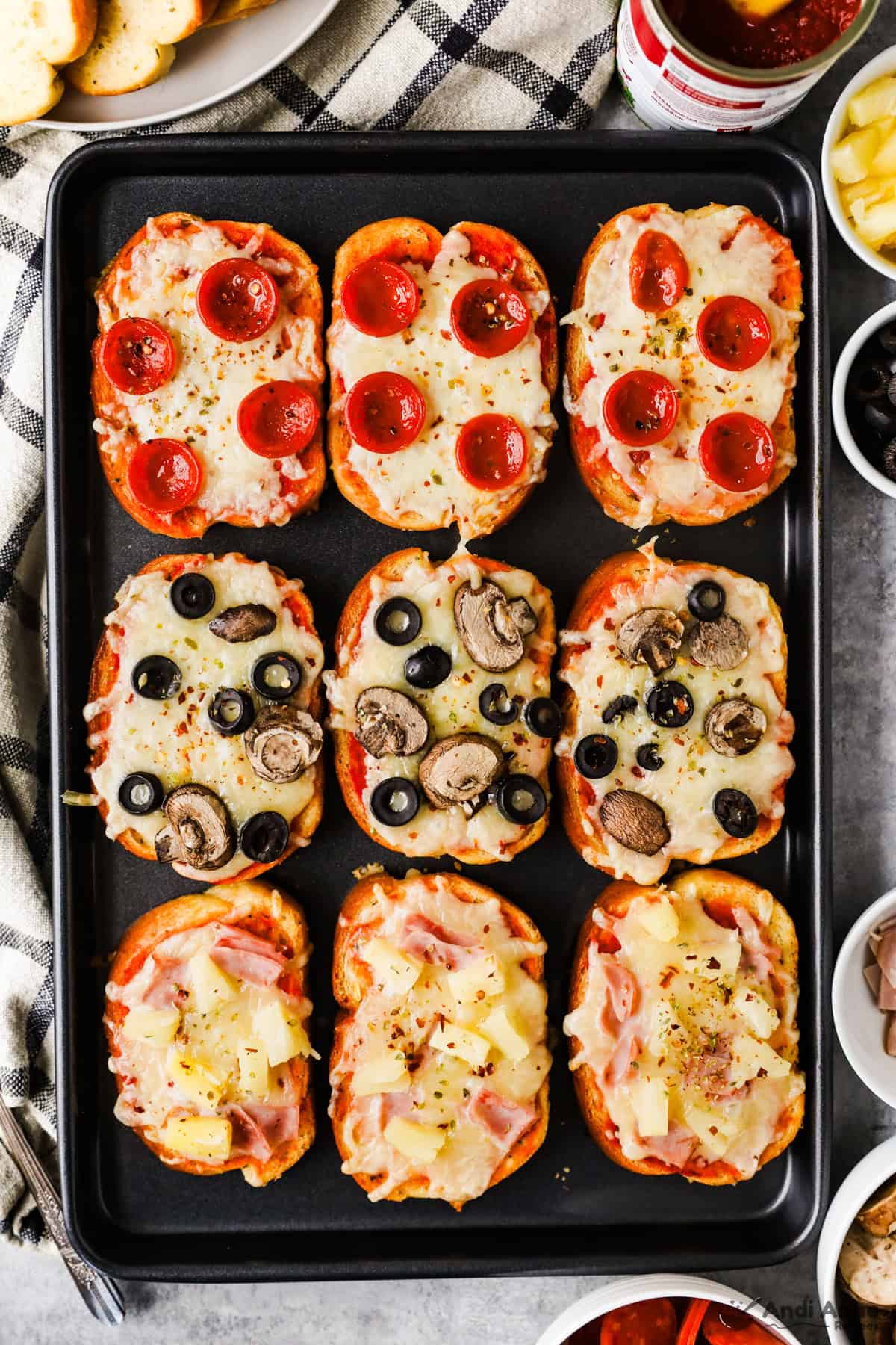 A baking sheet with pepperoni, olive and mushroom, and ham and pineapple garlic toast pizzas.