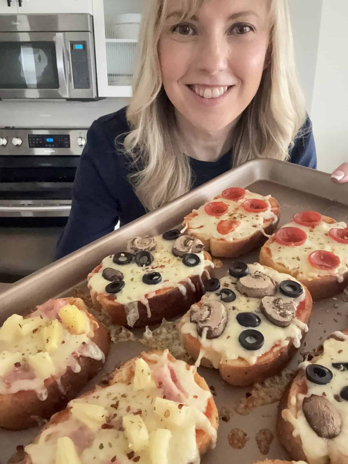 Andi is holding a baking tray of garlic bread pizzas.
