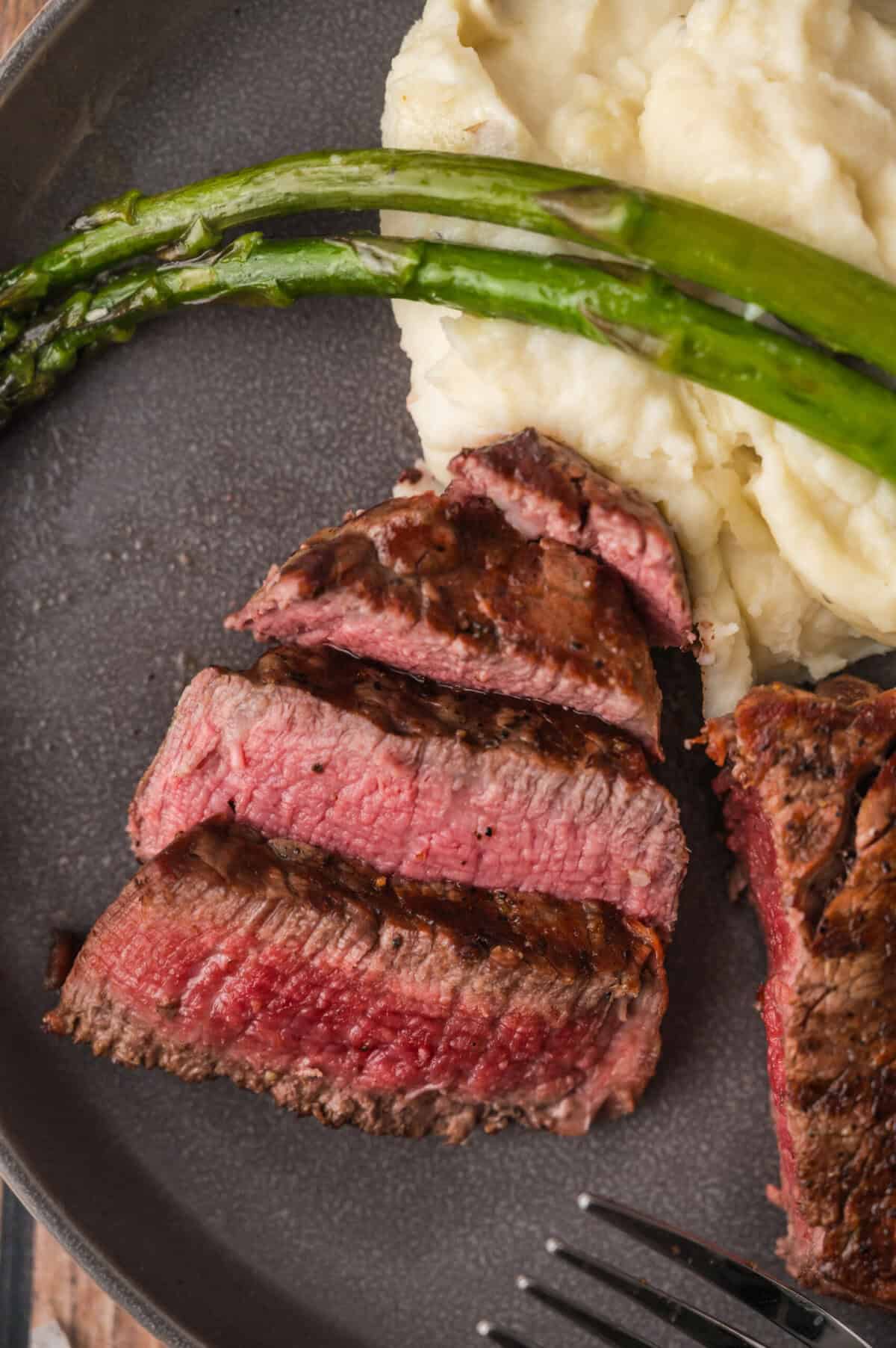 Grilled filet mignon is sliced and displayed on a plate with mashed potatoes and asparagus spears.