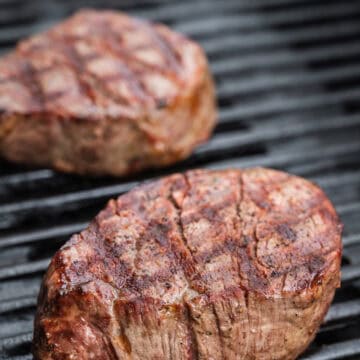 Two filet mignon steaks on a grill.