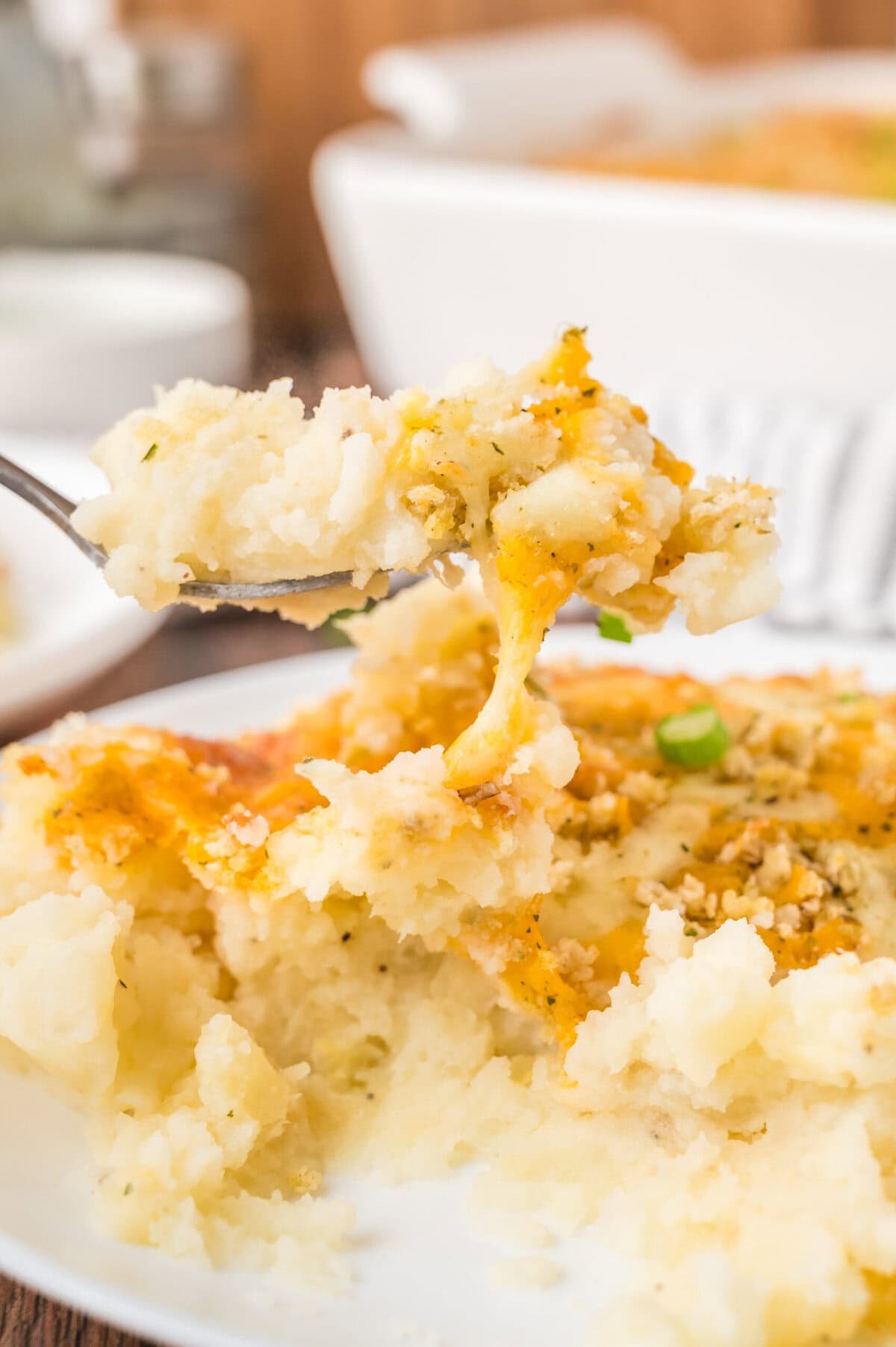 A fork full of cheesy mashed potato casserole.