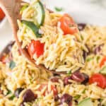 A wooden spoon is holding Mediterranean Orzo Salad.