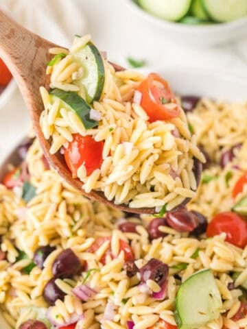 A wooden spoon is holding Mediterranean Orzo Salad.