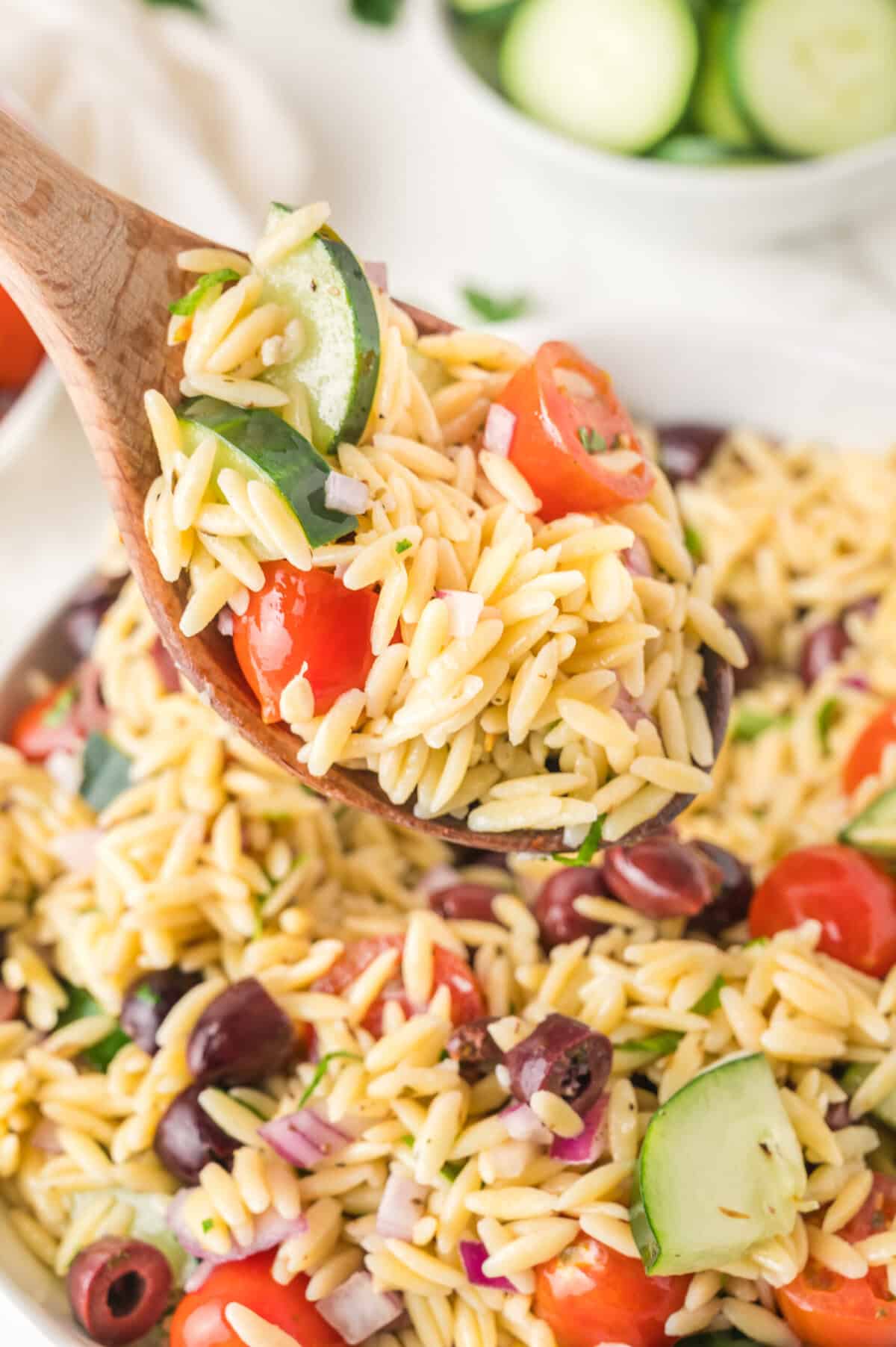 A wooden spoon is holding Mediterranean Orzo Salad.