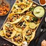 A tray full of sweet potato and black bean tacos with a side dish of avocado crema.
