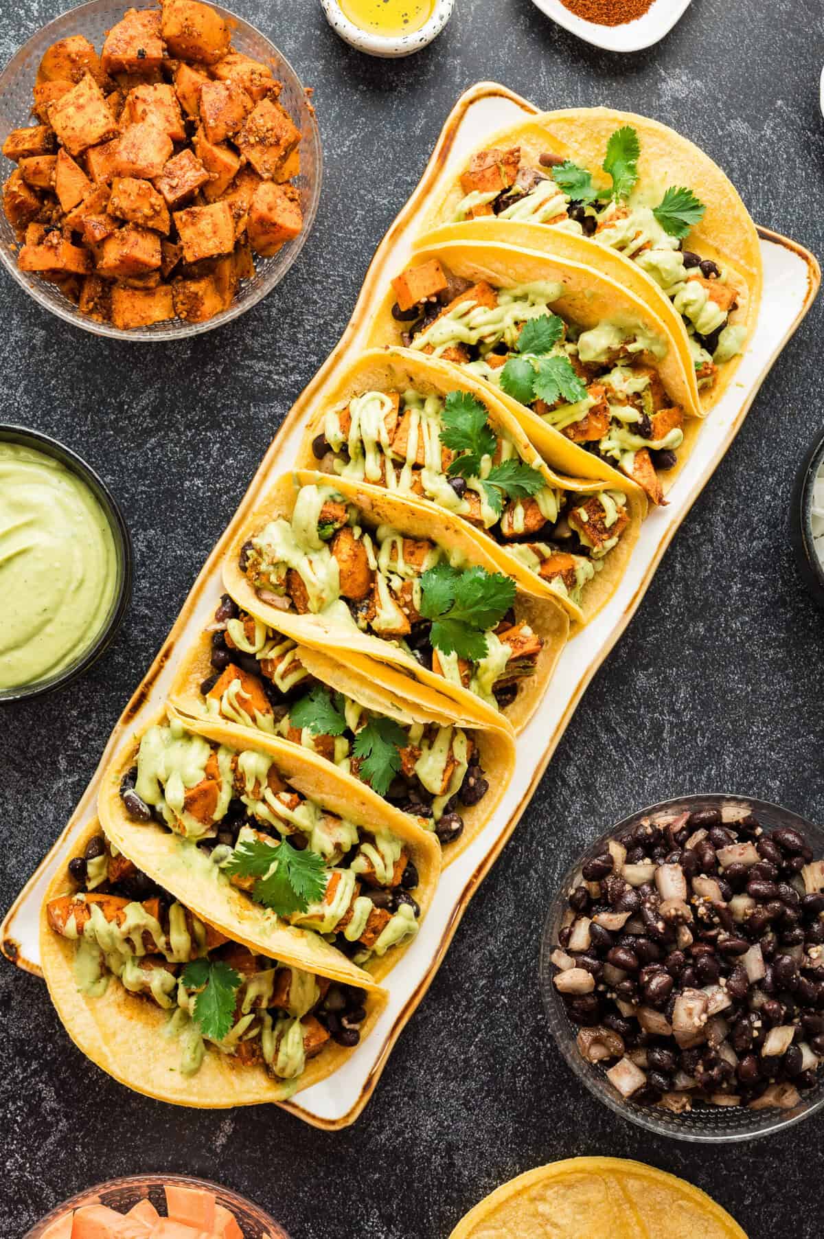 A serving tray filled with sweet potato and black bean tacos that are topped with avocado crema and cilantro.