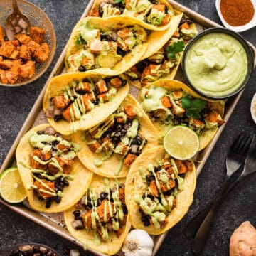 A tray full of sweet potato and black bean tacos with a side dish of avocado crema.