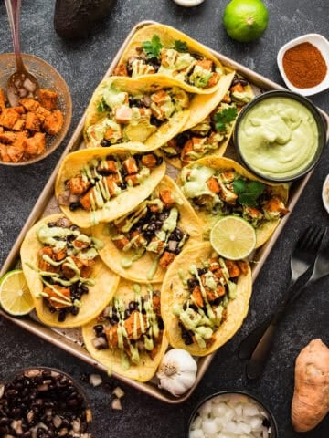 A tray full of sweet potato and black bean tacos with a side dish of avocado crema.