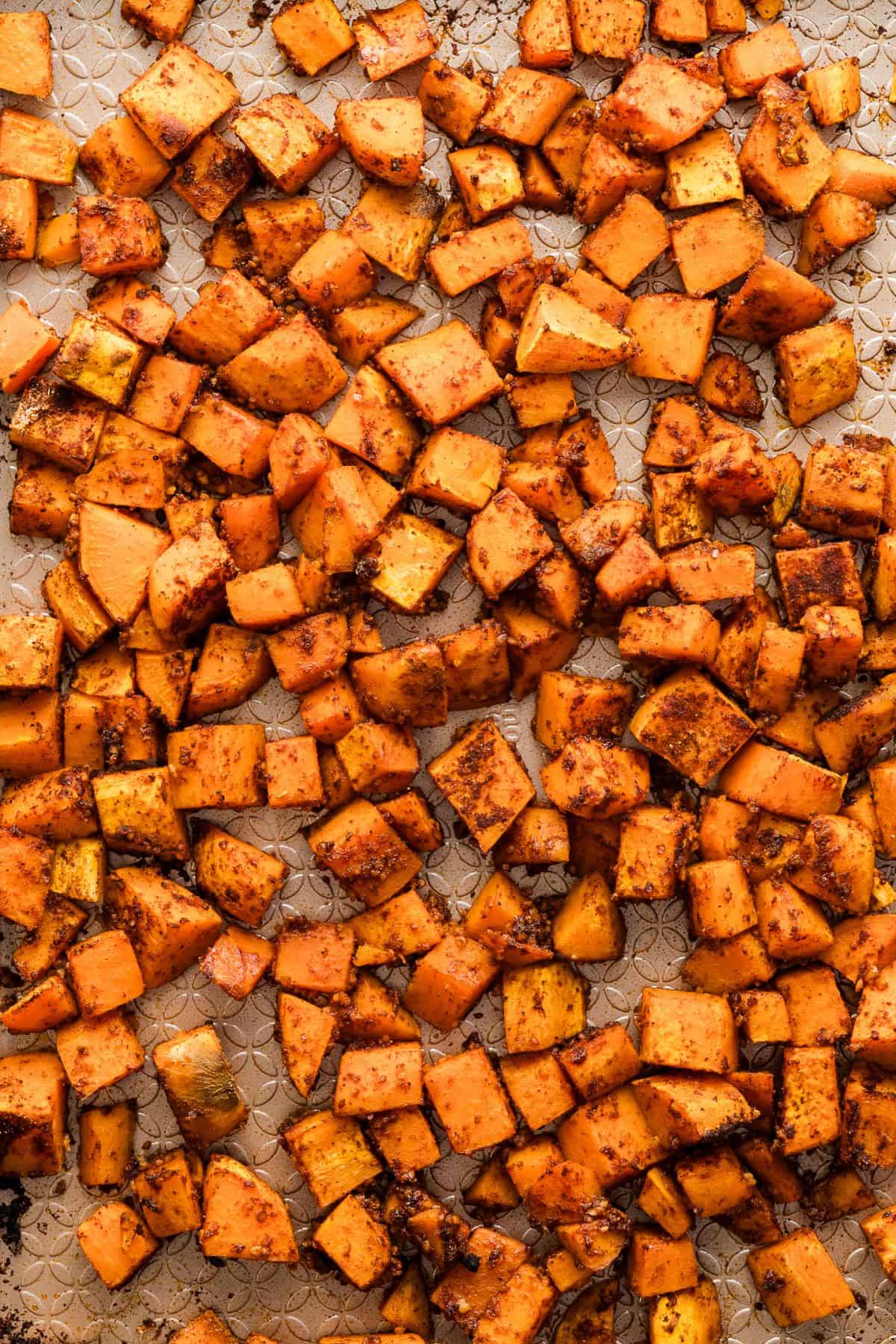 Roasted sweet potatoes with seasoning on a sheet pan.