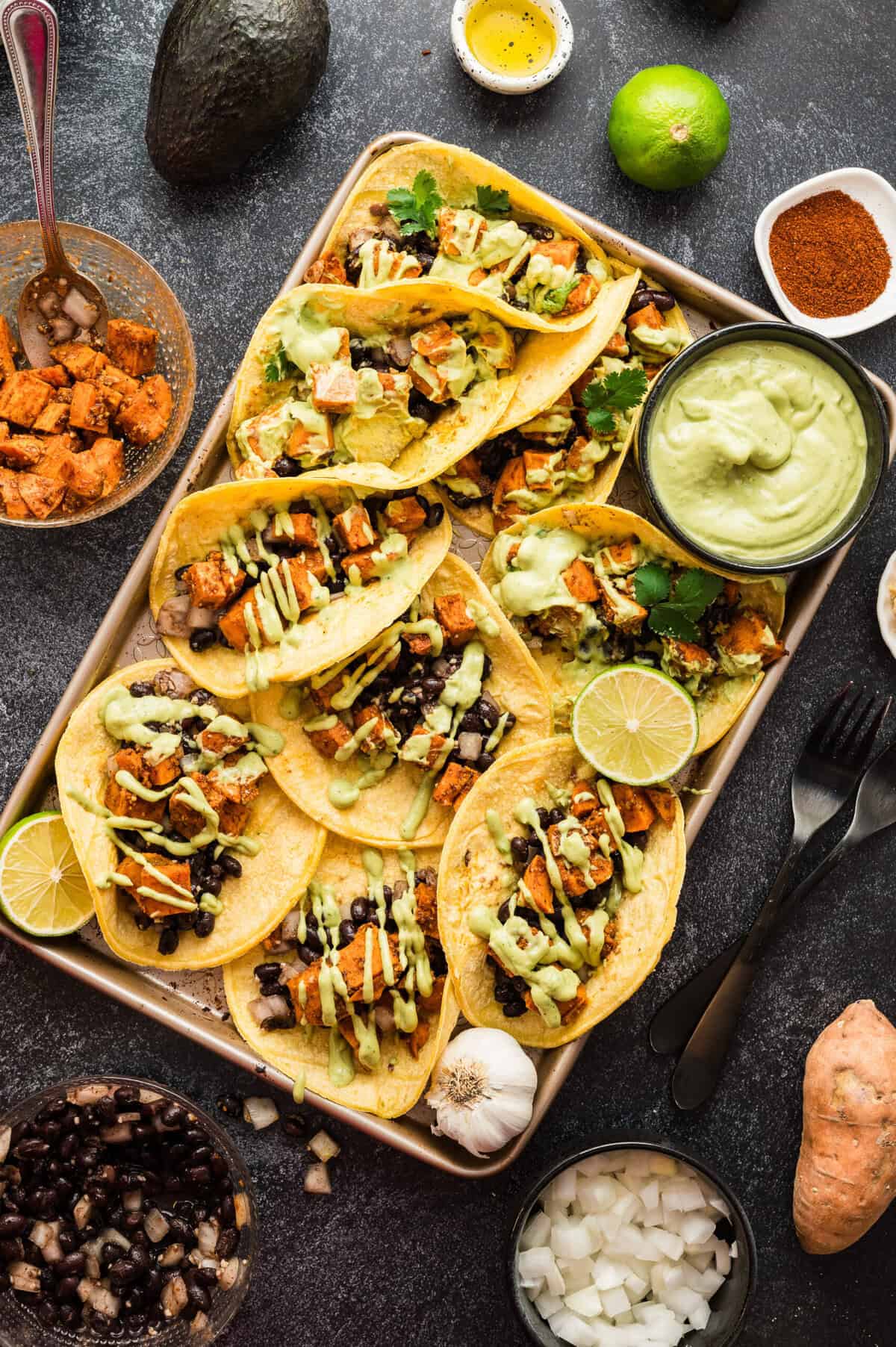 A tray full of sweet potato and black bean tacos with a side dish of avocado crema.