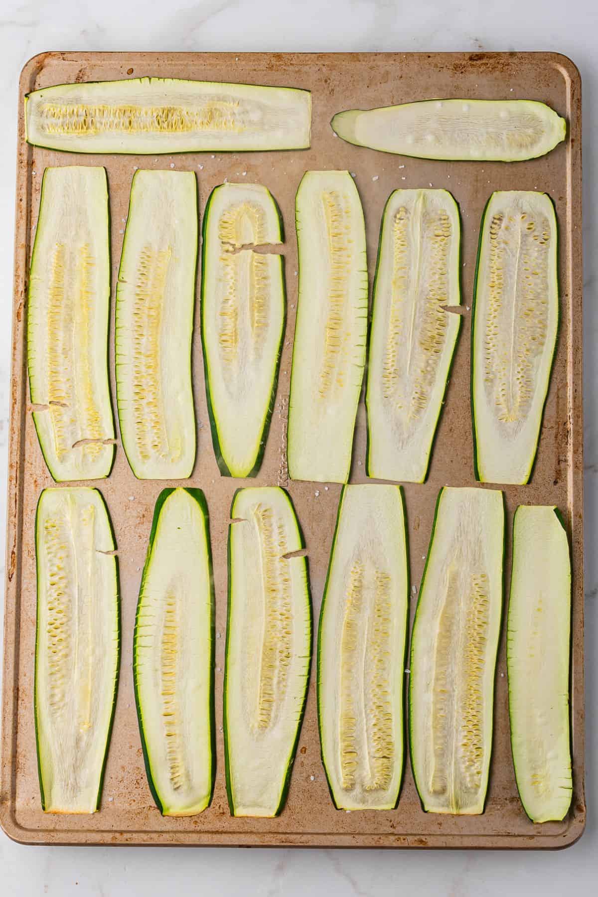 Slices of zucchini are laid out on a baking sheet and roasted.