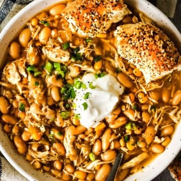 A large bowl of white chicken chili topped with sour cream and a bun on the side.