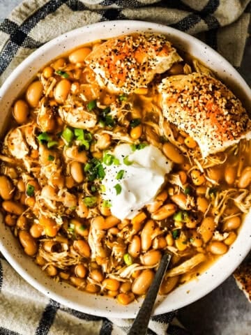 A large bowl of white chicken chili topped with sour cream and a bun on the side.