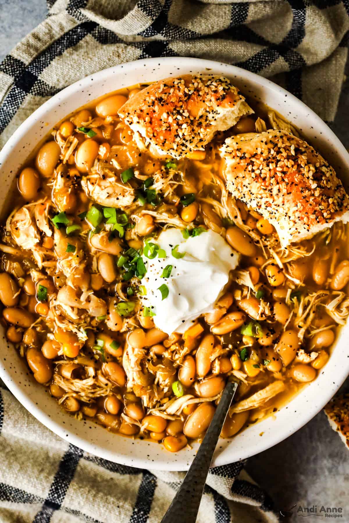 A large bowl of white chicken chili topped with sour cream and a bun on the side.