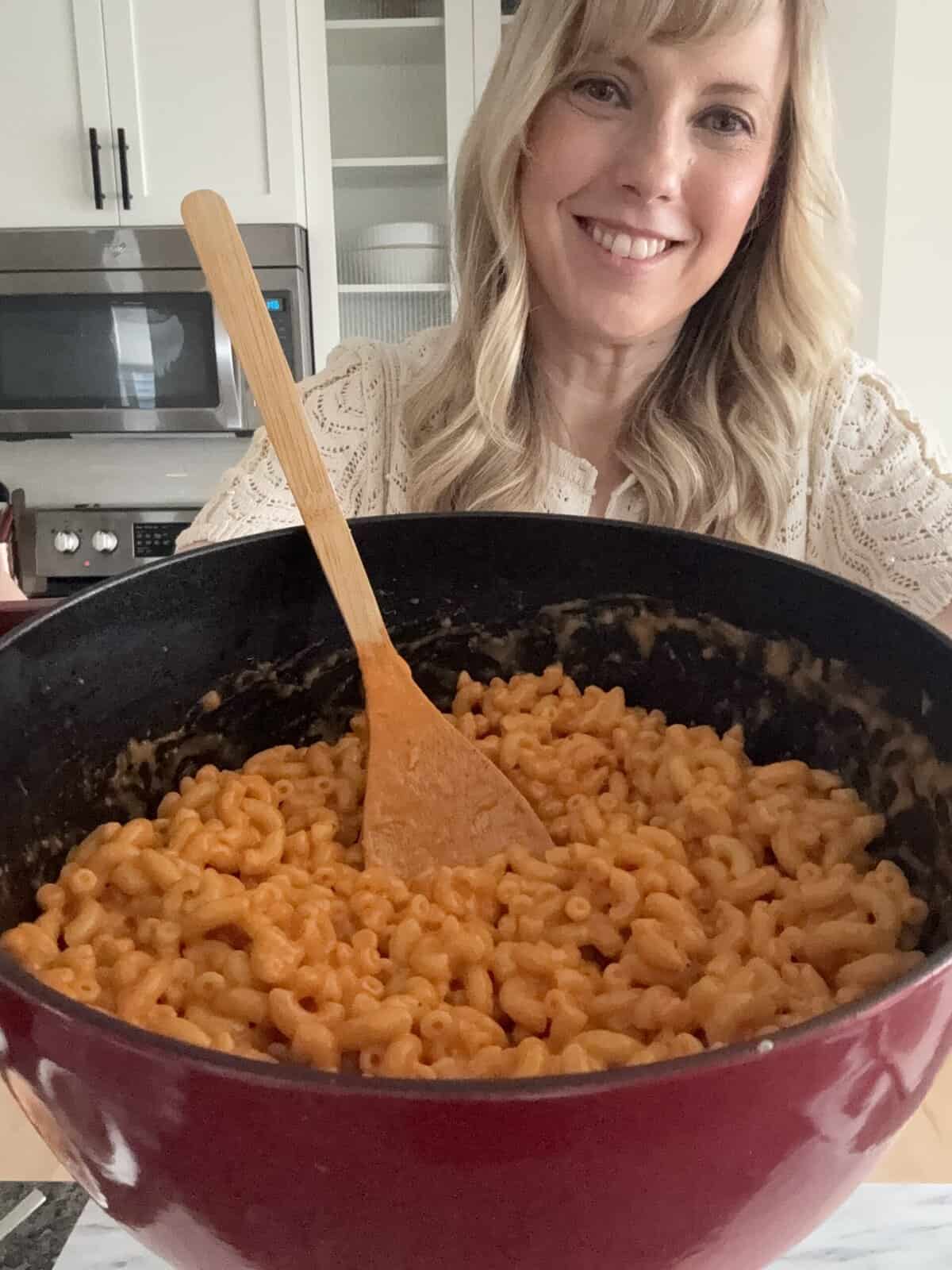 Andi is holding a large pot of mac and cheese made with tomato soup.