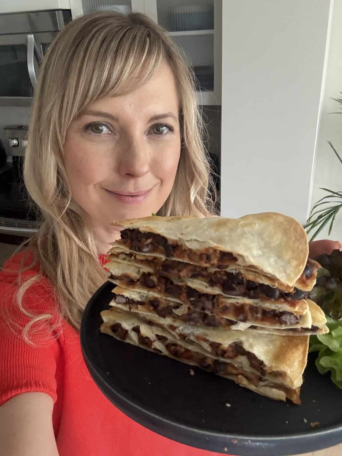 Andi is holding a stack of black bean quesadilla halves on a plate.
