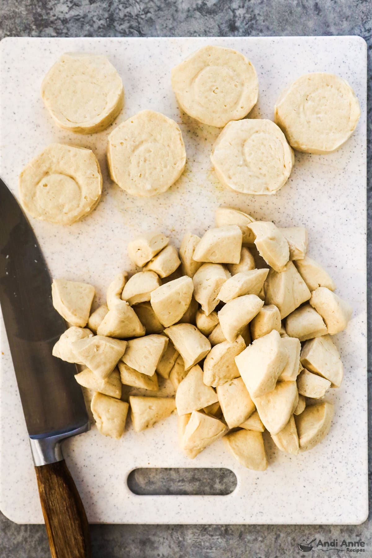 Canned fridge biscuits are chopped into chunks on a cutting board with a knife.