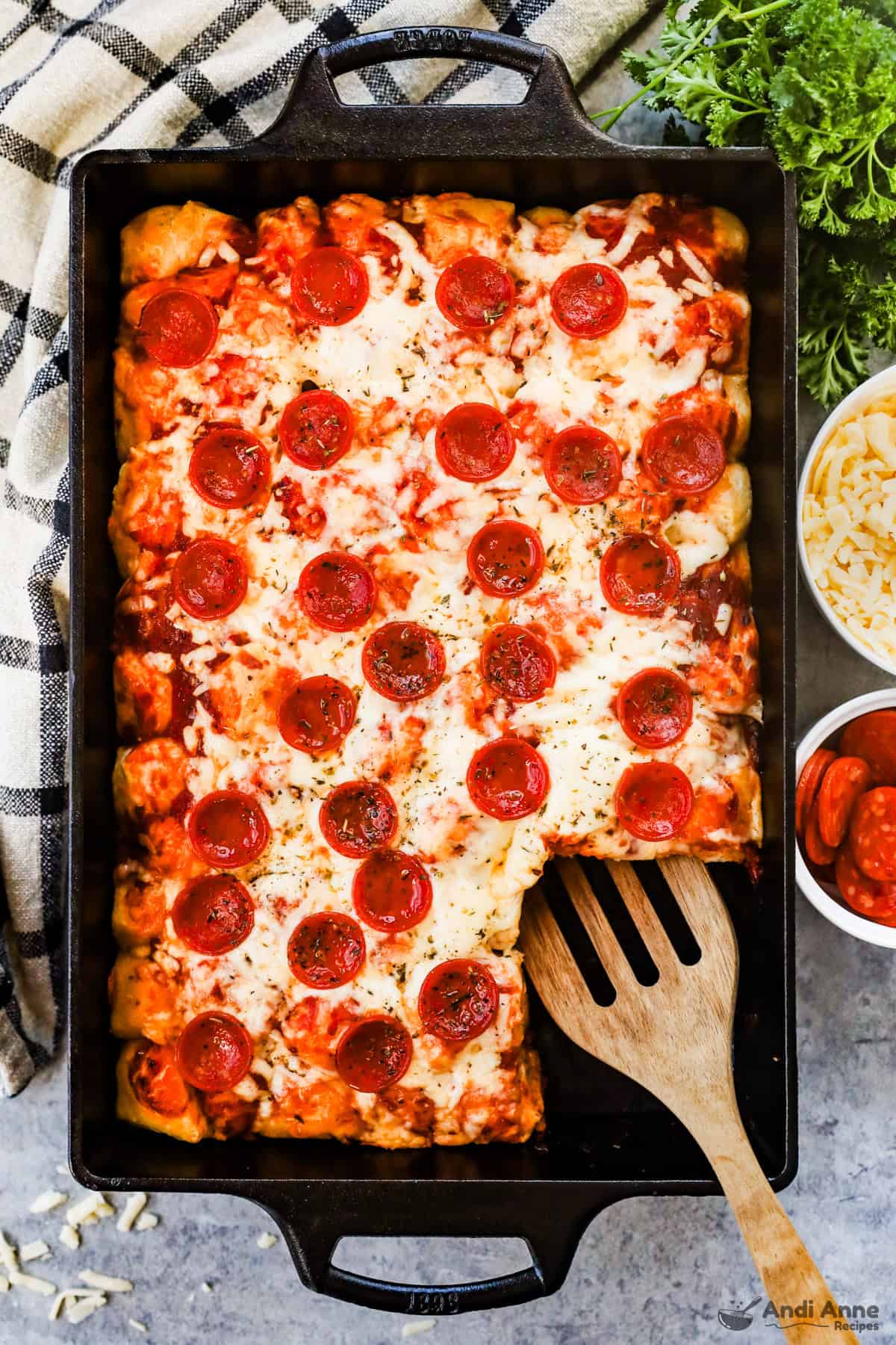 A pan filled with pizza biscuit casserole is on the counter with a slice removed.