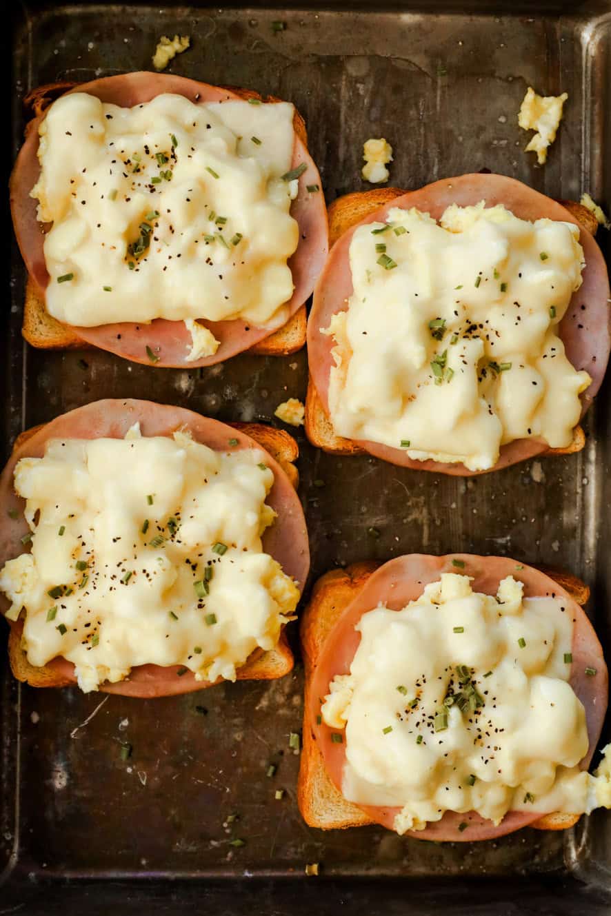 Slices of toast are topped with ham, scrambled eggs, and melted cheese.