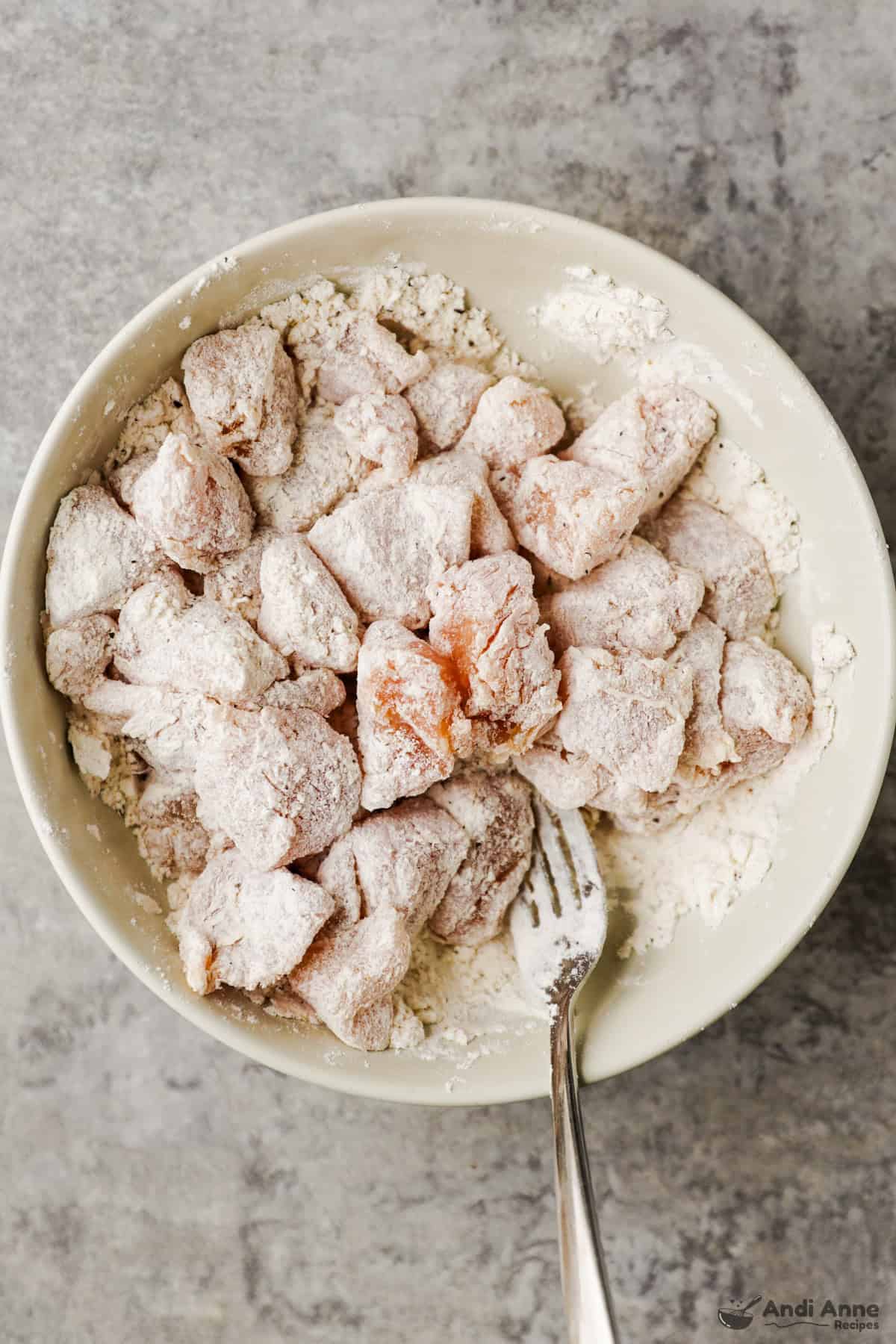 The chicken pieces are coated in flour in a bowl.