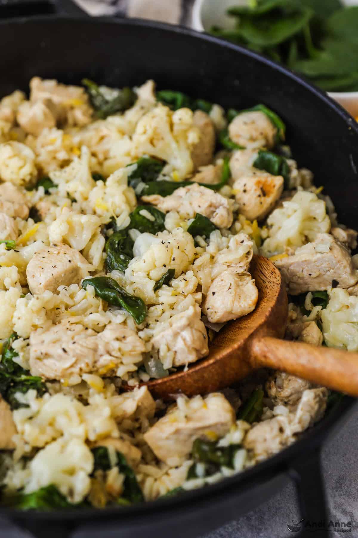 A skillet with chicken, rice, cauliflower, spinach, and lemon zest.