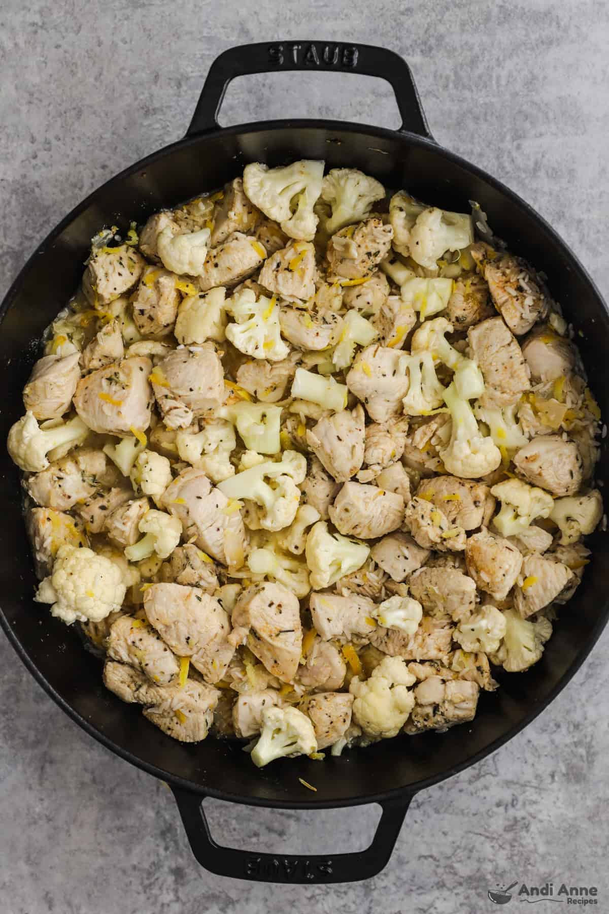 Cauliflower, rice, lemon juice, lemon zest, and chicken broth are added to the chicken in a skillet.