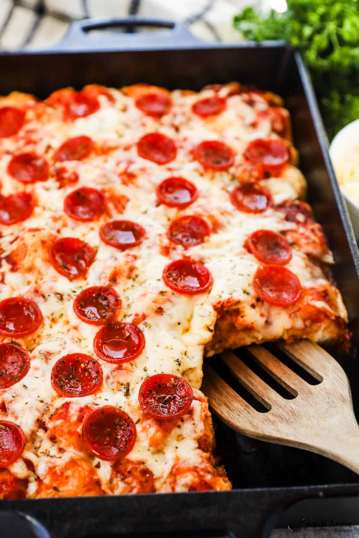 Biscuit pieces mixed with pizza sauce, pepperoni slices, and cheese in a casserole dish, with a slice removed.