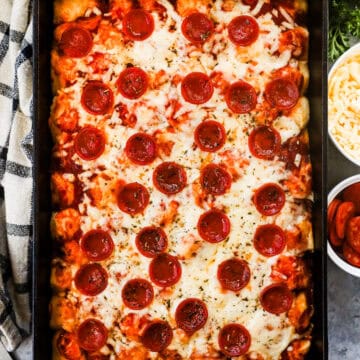 Biscuit pieces mixed with pizza sauce, pepperoni slices, and cheese in a casserole dish.