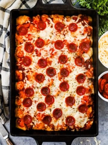 Biscuit pieces mixed with pizza sauce, pepperoni slices, and cheese in a casserole dish.