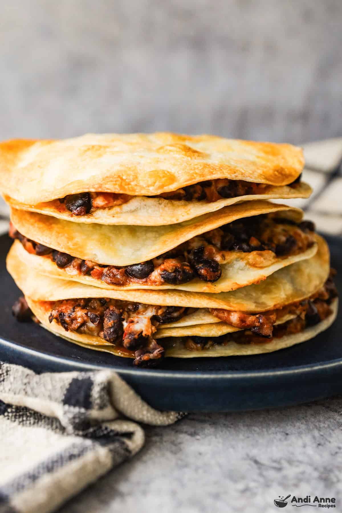 A stack of flour tortillas filled with black beans, melted cheese, and salsa.