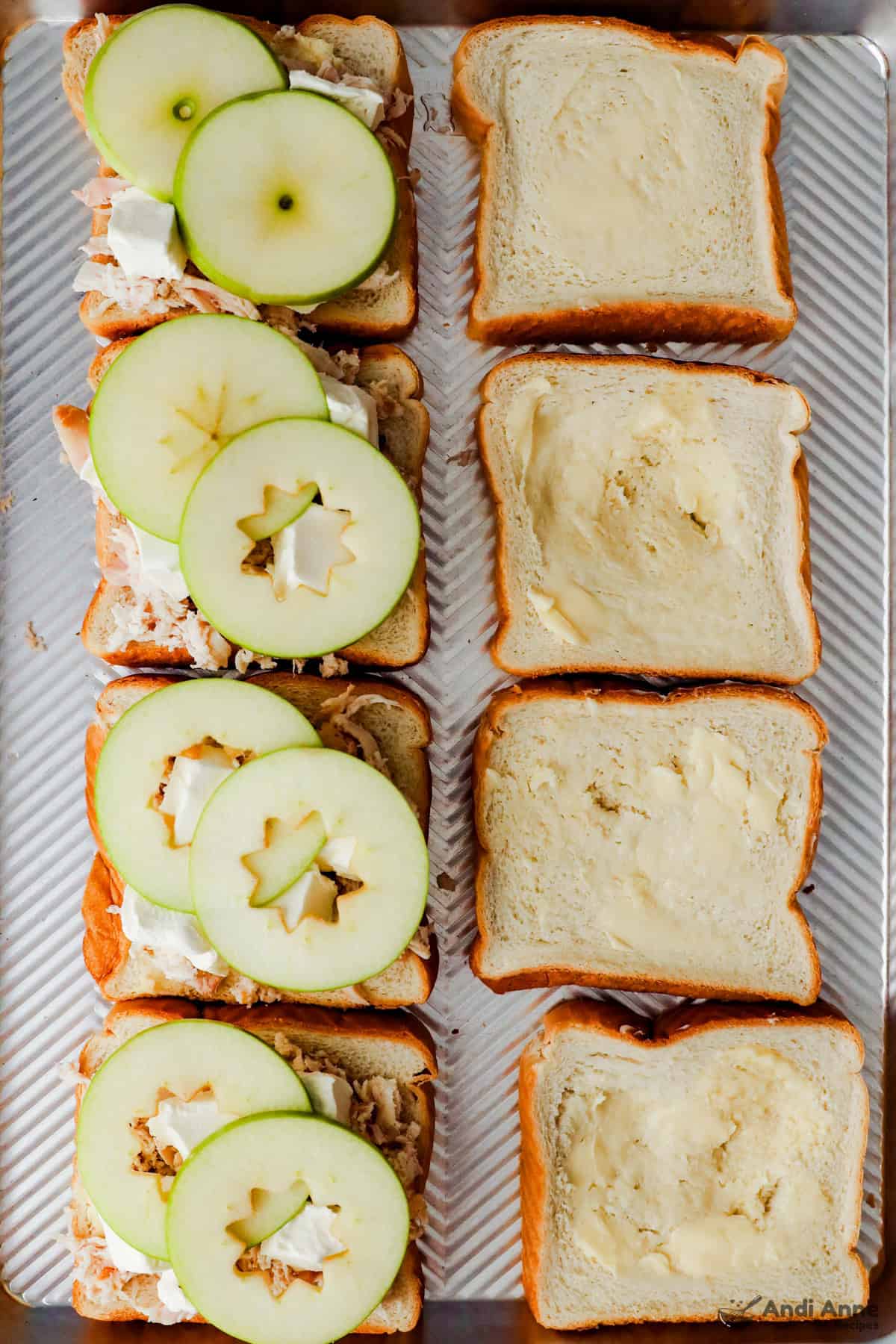 A slice of buttered bread is topped with shredded rotisserie chicken, a slice of cream cheese and a slice of Granny Smith apple