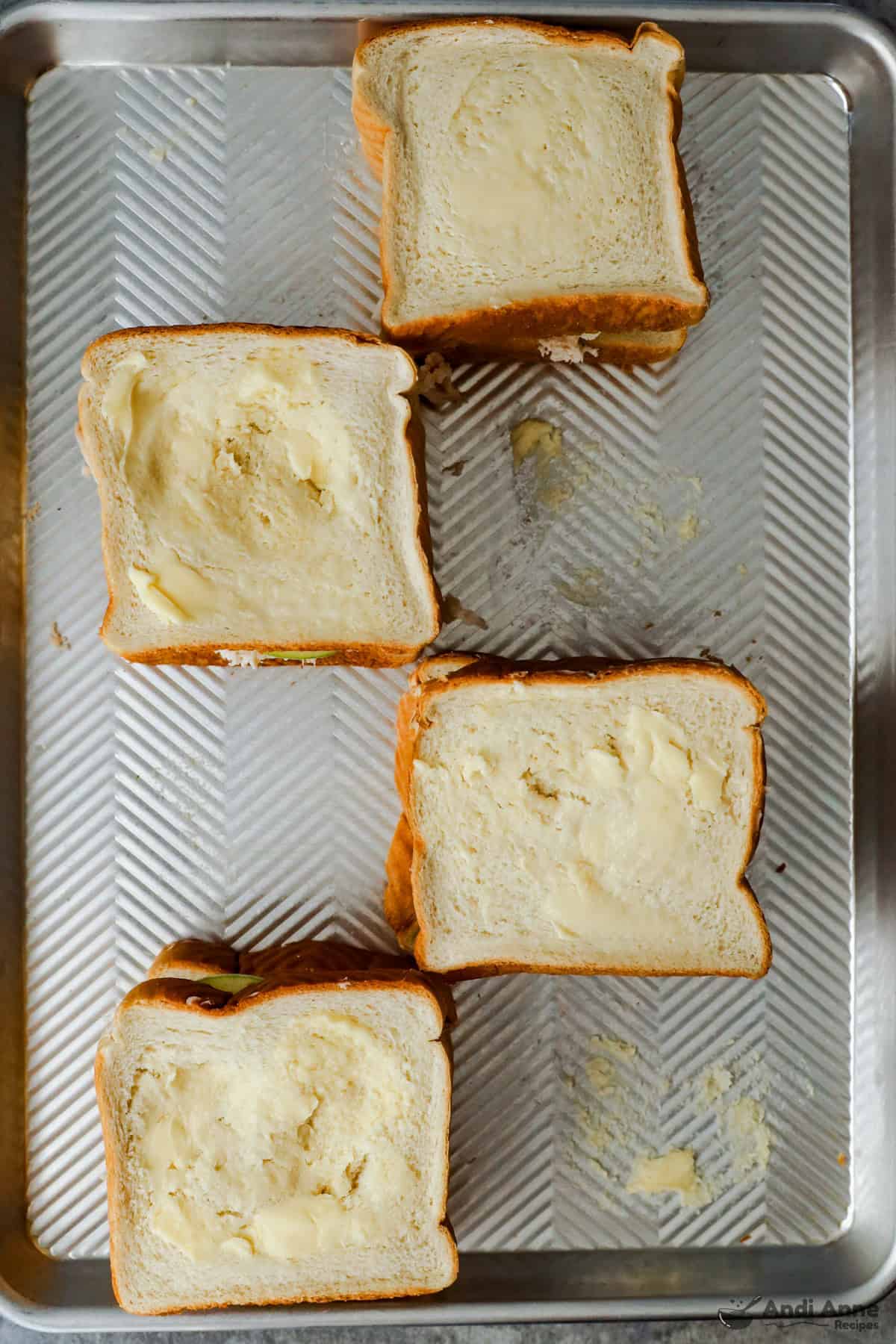 A slice of buttered bread is topping the chicken and apple sandwiches on a baking tray.