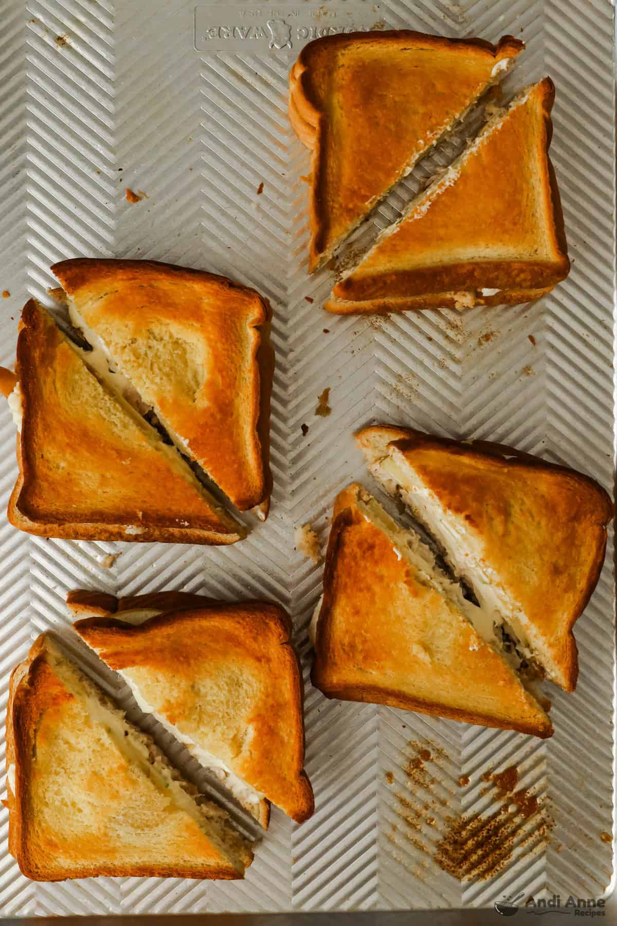 Toasted and sliced chicken and apple sandwiches on a baking tray.