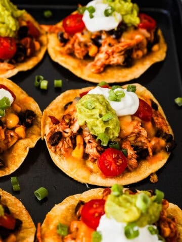 Crispy corn tostadas topped with rotisserie chicken, beans, corn, salsa, sour cream, guacamole, and green onions.
