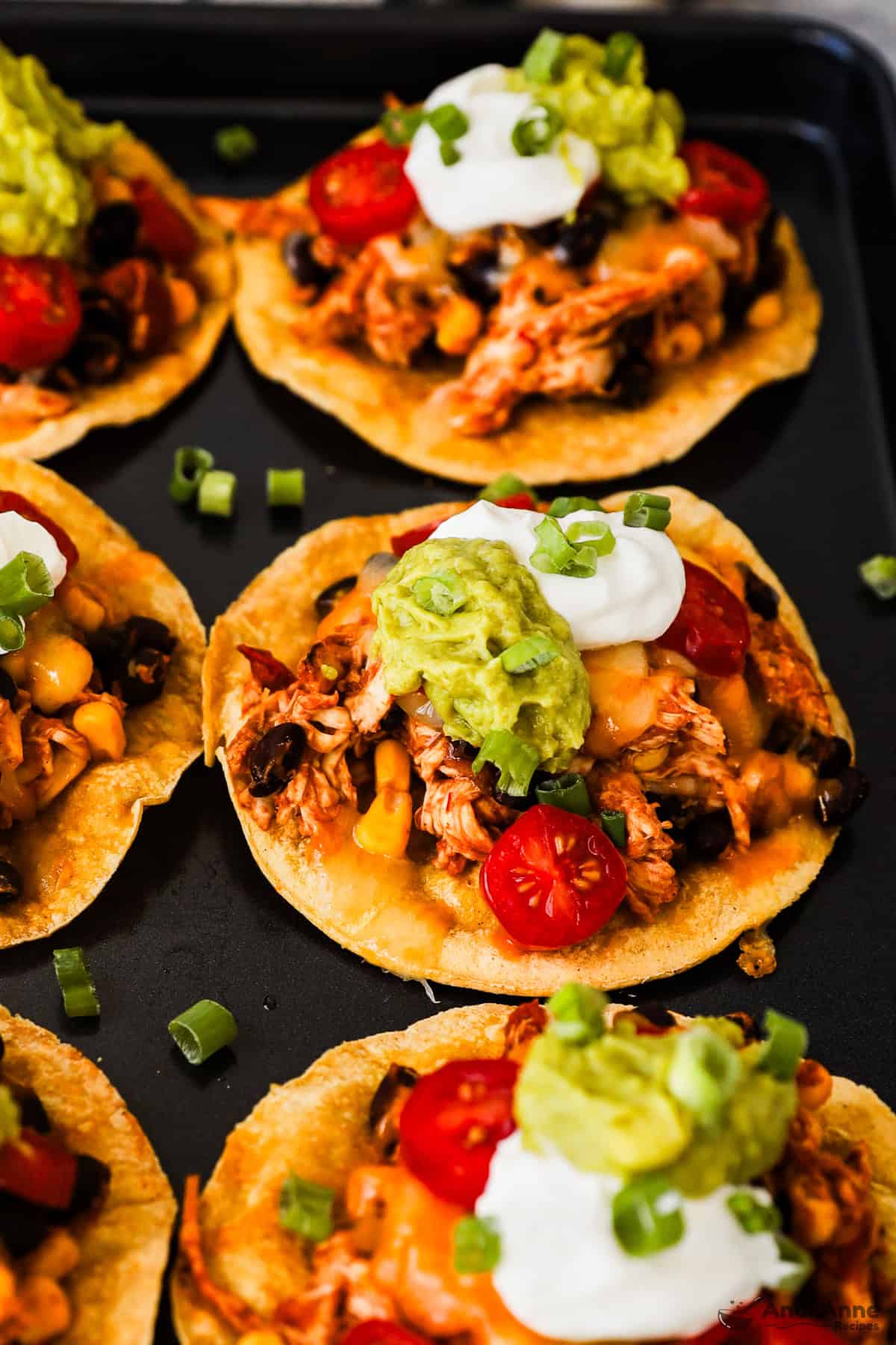 Crispy corn tostadas topped with rotisserie chicken, beans, corn, salsa, sour cream, guacamole, and green onions.