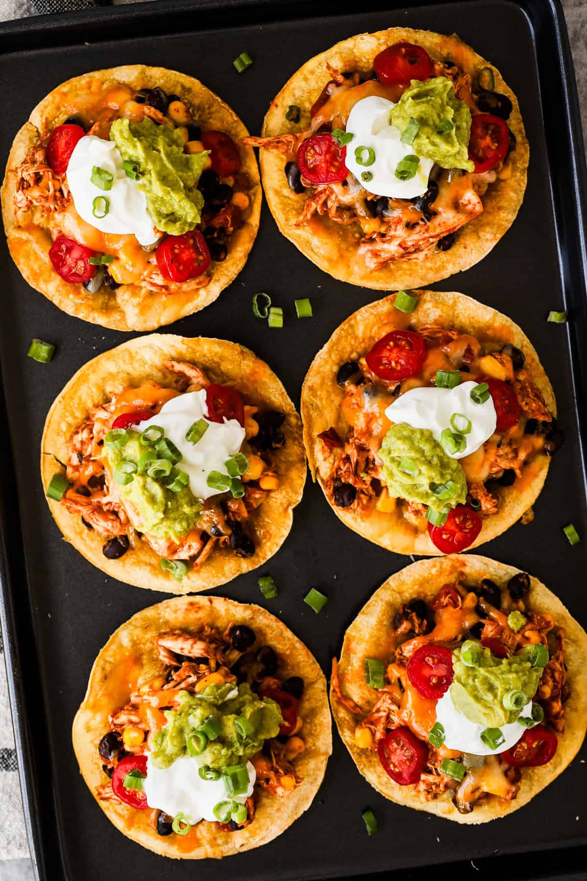 Crispy corn tostadas topped with rotisserie chicken, beans, corn, salsa, melted cheese, sour cream, guacamole, and green onions.