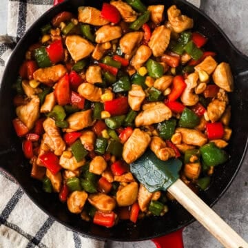 Kung pao chicken in a skillet with red and green bell peppers.