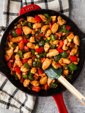 Kung pao chicken in a skillet with red and green bell peppers.