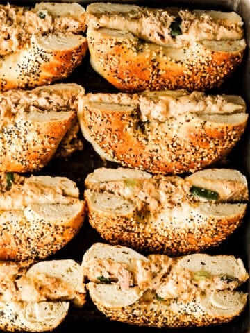 Tuna melt bagels cut in half on a sheet pan.