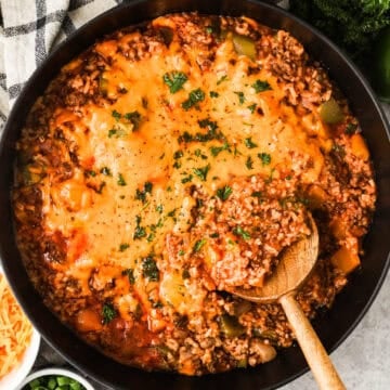 A skillet with ground beef, rice, bell peppers, and tomato sauce topped with melted cheese.
