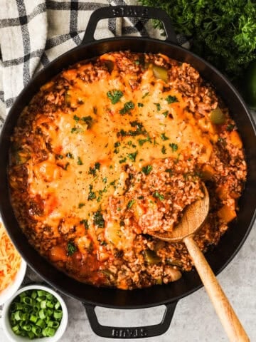 A skillet with ground beef, rice, bell peppers, and tomato sauce topped with melted cheese.